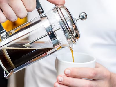 Barista nalévá filtrovanou kávu z french pressu do bílého šálku